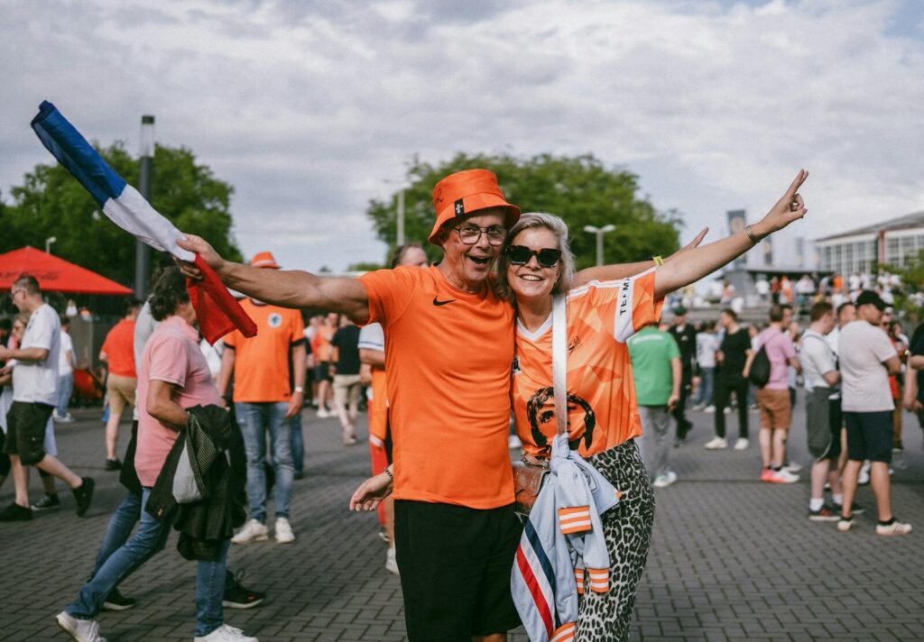 Enthusiastic fans in orange outfits celebrating together with flags at an outdoor event.
